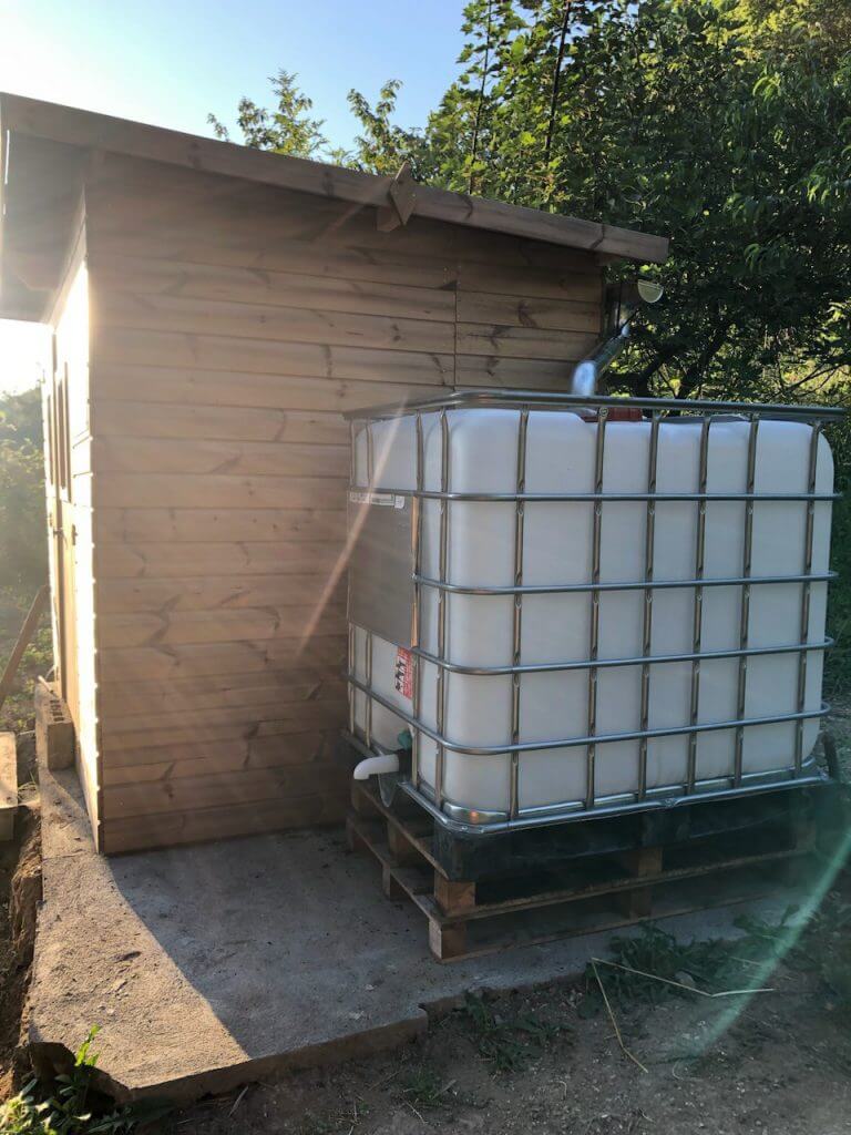 Cuve IBC de 1000 litres, branchée à une gouttière. et équipée d'un bec de vidange.